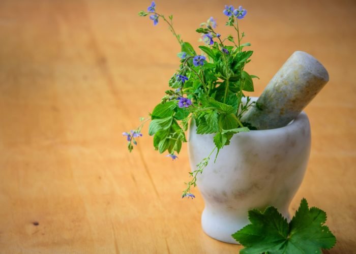 Marble mortar and pestle with fresh herbs and flowers on wooden table enhancing natural health and cooking aesthetics.